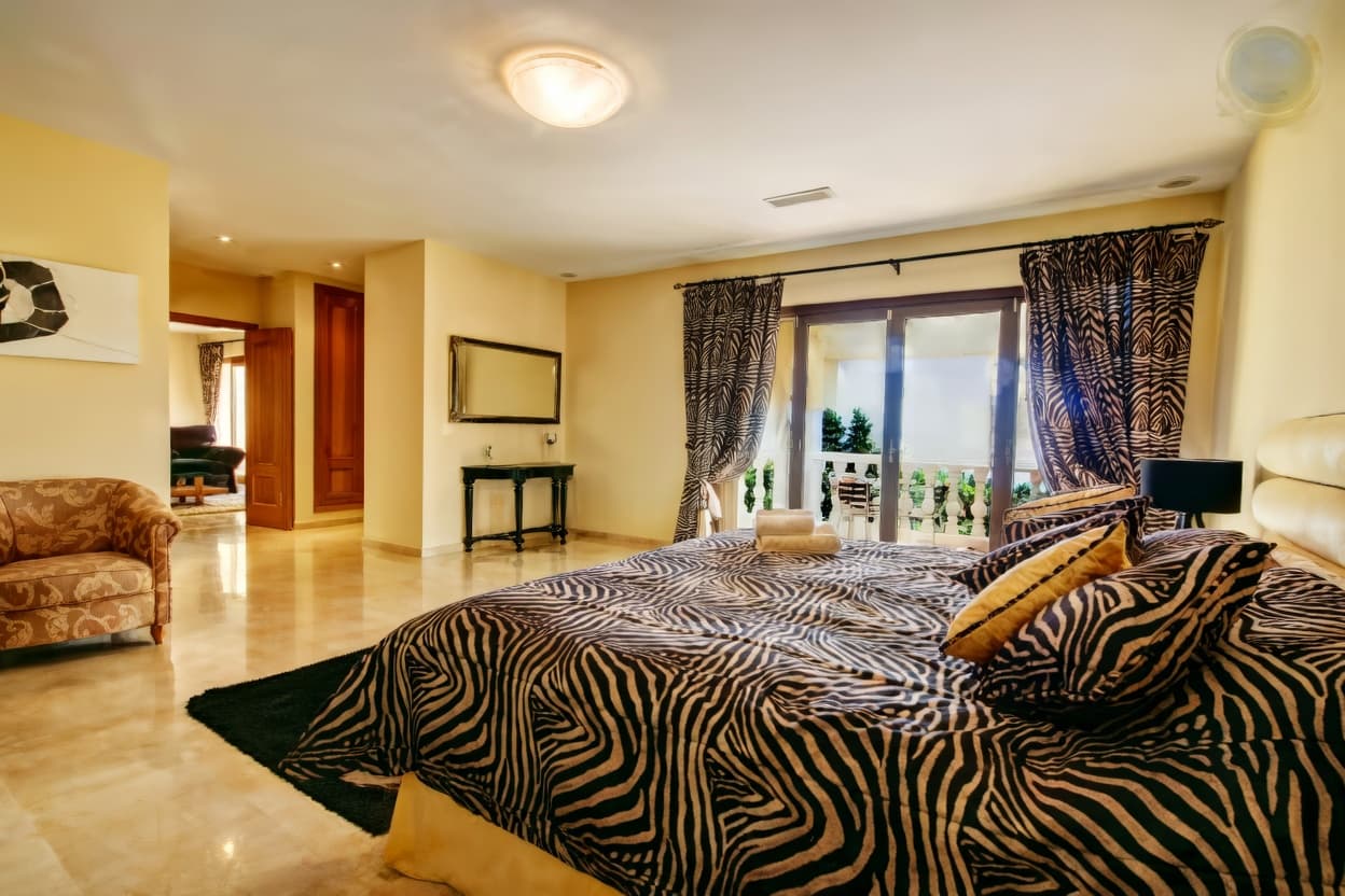 Habitación con cama de cebra, cortinas a juego, sillón y suelos de mármol brillante.