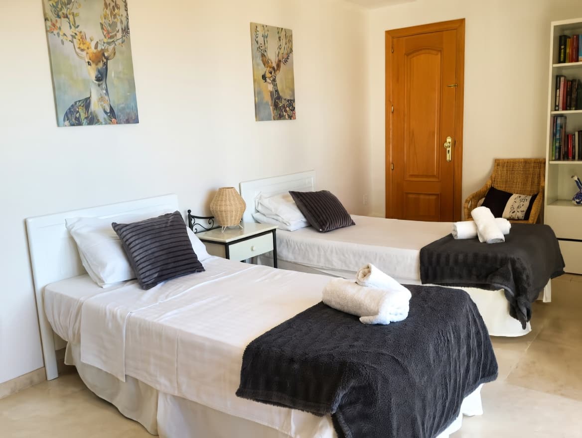 Dos camas individuales con sábanas blancas, mantas grises y toallas, bajo cuadros decorativos de ciervos.